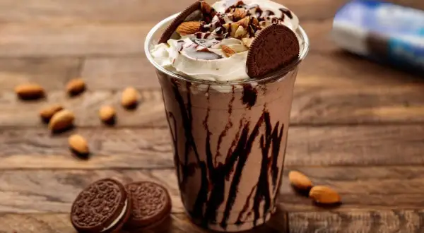Un délicieux milkshake vegan au chocolat, garni de crème, d'amandes et de biscuits, sur fond de bois.