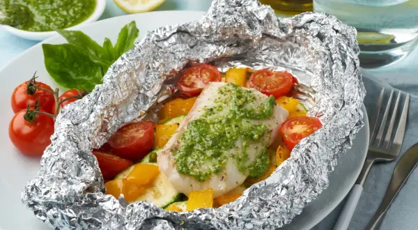 Un délicieux poisson en papillote, garni de légumes colorés et d'une sauce verte savoureuse, prêt à être dégusté.