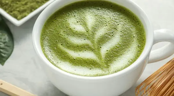 Un délicieux café matcha latte, orné d'une mousse crémeuse et d'une pincée de poudre de matcha sur une cuillère en bois.