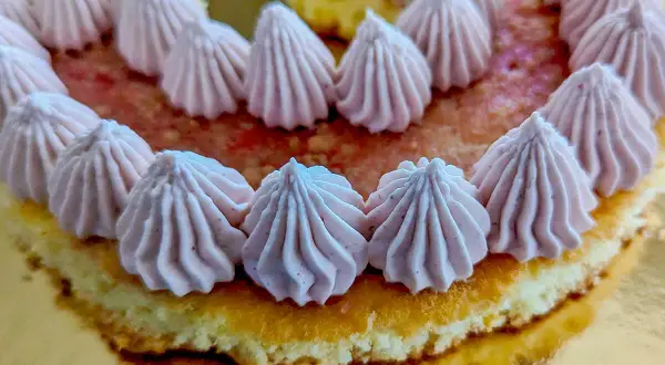 Gâteau orné de rosaces de ganache chocolat blanc framboise sur un lit de fruits rouges.