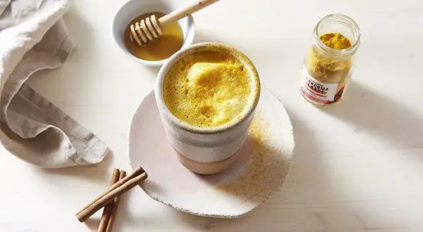 Un golden latte crémeux, prêt à déguster. Découvrez les golden latte bienfaits pour une pause réconfortante et saine. Miel et curcuma à portée de main.