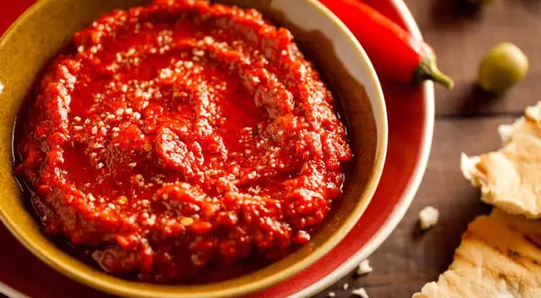 Un bol de harissa maison, prêt à être dégusté avec du pain pita. Une recette simple pour un goût authentique.