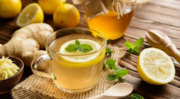 Une tasse de thé chaud au citron et à la menthe, avec du ginseng gingembre râpé, des citrons entiers et un pot de miel.