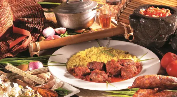Un rougail saucisses traditionnel, servi avec du riz jaune, des tomates, des oignons et des épices.