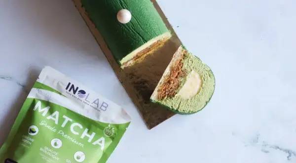 Bûche glacée verte au matcha, garnie d'une ganache matcha crémeuse et d'une surprise au centre. À côté, un paquet de poudre de matcha de qualité premium.