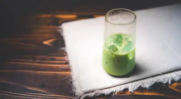 Un verre de matcha glacé sur un tissu blanc, sur fond de bois sombre. Une boisson rafraîchissante pour se demander : peut-on boire du matcha le soir ?