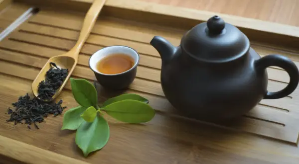 Service à thé en bambou avec théière noire, tasse de thé ambré, feuilles de thé et une branche de feuilles vertes. Parfait pour un thé sans théine.