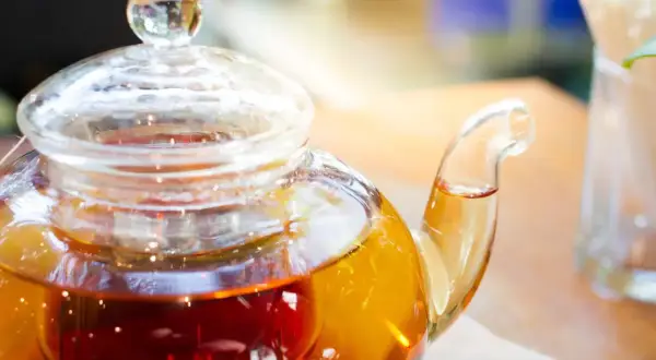 Thé ambré dans une théière en verre, prêt à être servi. La question est : combien d'eau pour un sachet de thé ?