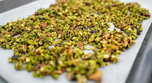 Granola claire au matcha, parsemée d'amandes et de graines, prête à être cuite sur une plaque de cuisson.
