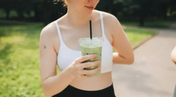 Une jeune femme aux taches de rousseur tient une boisson verte glacée, un rituel quotidien pour elle : boire du matcha.