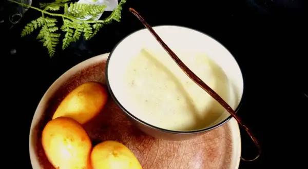 Un bol de lait vanille onctueux, garni d'une gousse de vanille, avec des madeleines dorées sur une assiette.
