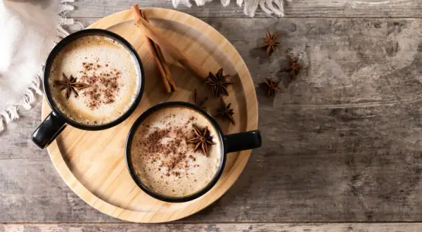 Deux tasses de chai latte réconfortant, garnies d'anis étoilé et de cannelle, sur un plateau en bois.