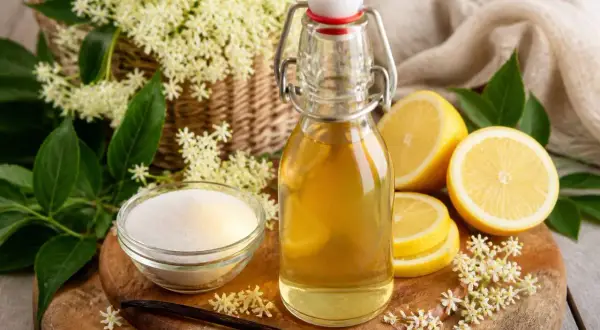 Bouteille de sirop de sureau, citrons, sucre et fleurs de sureau sur une planche en bois.