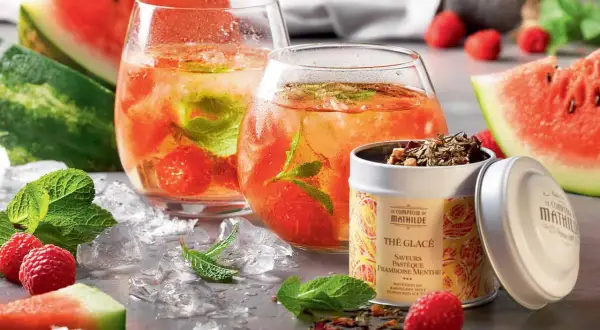 Deux verres de thé glacé maison aux fruits rouges et menthe, accompagnés de pastèque, framboises et d'une boîte de thé.