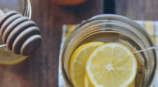 Un verre rempli de rondelles de citron, prêt à recevoir du miel et de la cannelle pour ses bienfaits.