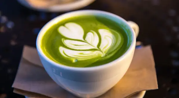 Un délicieux matcha lait d'avoine avec un art latte en forme de feuille, servi dans une tasse blanche sur une soucoupe.
