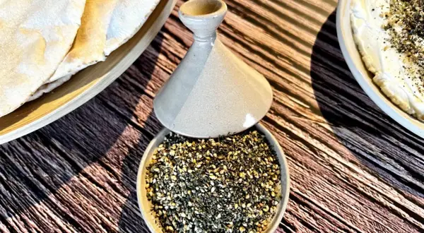 Un bol de zaatar prêt à être utilisé pour une recette, avec du pain pita et une trempette crémeuse.