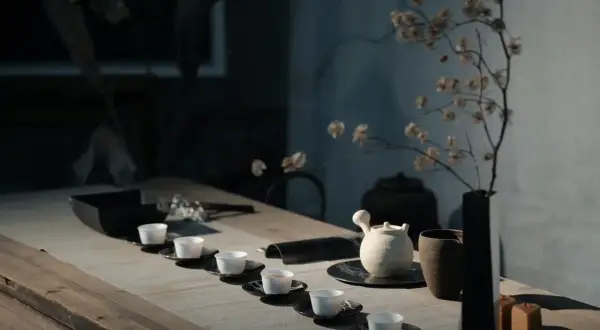 Service à thé minimaliste avec tasses blanches alignées. Une théière en céramique et un vase de fleurs séchées évoquent l'art de comment conserver le thé.