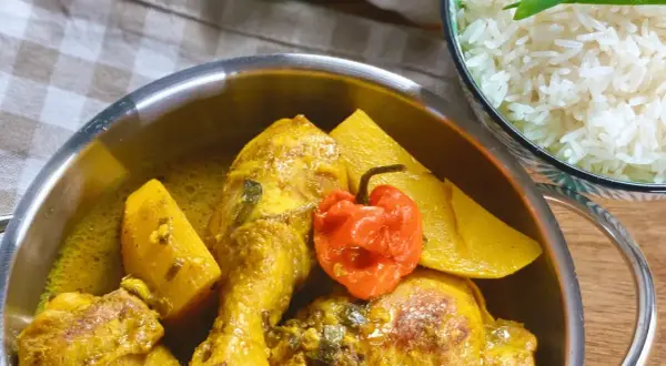 Un plat de poulet au curry, parfumé par l'épice colombo, avec des morceaux de patate douce et un piment rouge. Servi avec du riz blanc.