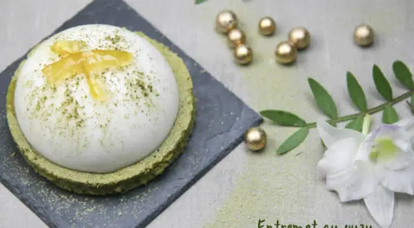 Un entremet yuzu aérien, saupoudré de matcha, repose sur un financier au thé matcha. Décoré de zestes de yuzu confits.