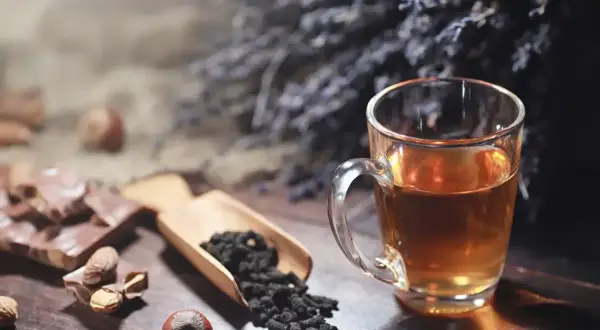 Un thé ambré dans une tasse, du chocolat, des noisettes et des feuilles de thé. Idéal pour le temps conservation thé infusé.