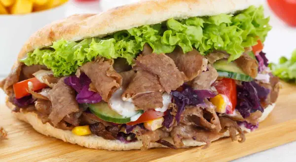 Un généreux kebab maison garni de viande, salade, tomates, concombre et chou rouge, prêt à être dégusté.