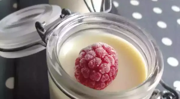 Délicieux panna cotta chocolat blanc, garni d'une framboise givrée, dans un pot en verre.