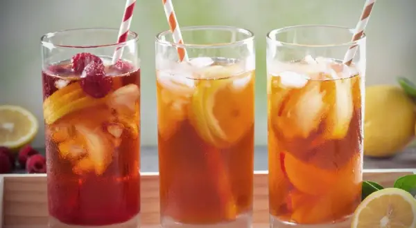 Trois verres de thé vert glacé, garnis de fruits rouges et de citron, prêts à être dégustés.