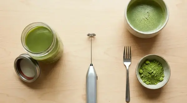 Préparation du matcha sans fouet : poudre verte, boisson mousseuse dans un bol, et un petit appareil argenté pour mélanger.