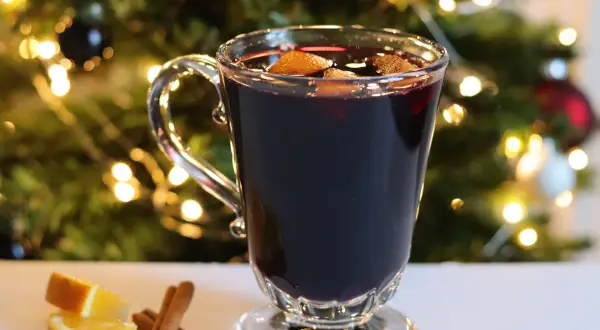 Verre de vin chaud sans alcool, garni d'orange et de cannelle, devant un sapin de Noël illuminé. Parfait pour une recette festive et réconfortante.