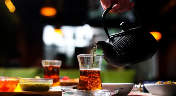 Une main verse du thé ceylan bienfait dans un verre. Ambiance chaleureuse et réconfortante.