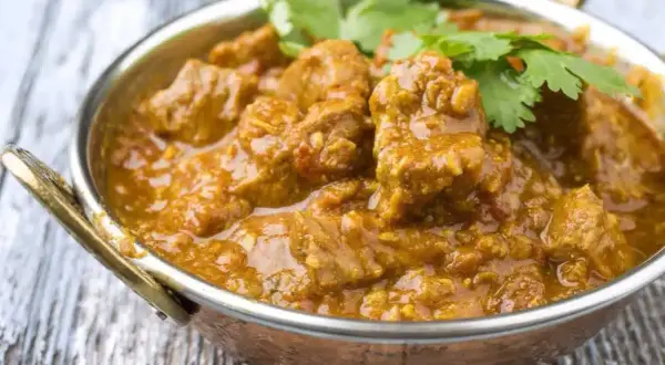 Un savoureux colombo d'agneau, mijoté dans une sauce épicée et garni de coriandre fraîche, servi dans un bol en cuivre.