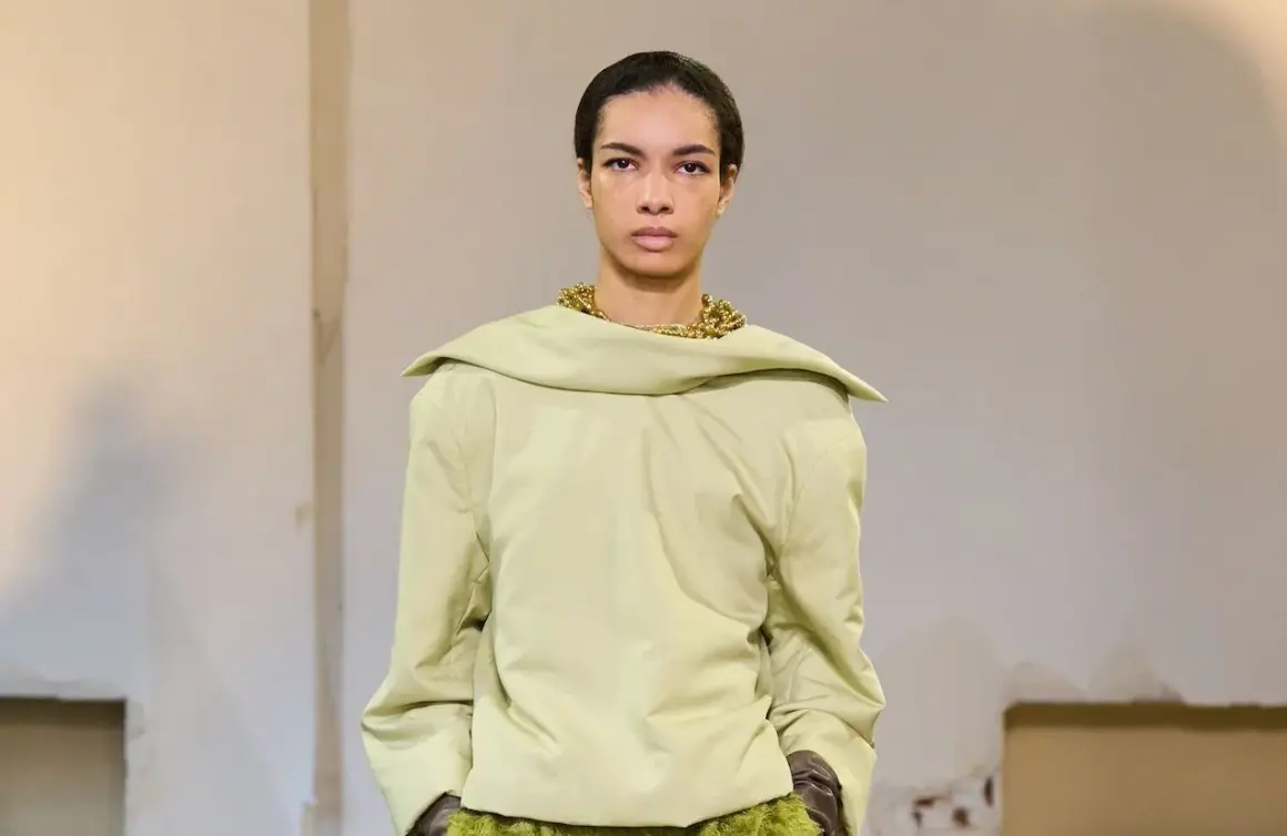 Mannequin portant un haut ample couleur matcha, avec un collier doré audacieux et une jupe texturée verte.
