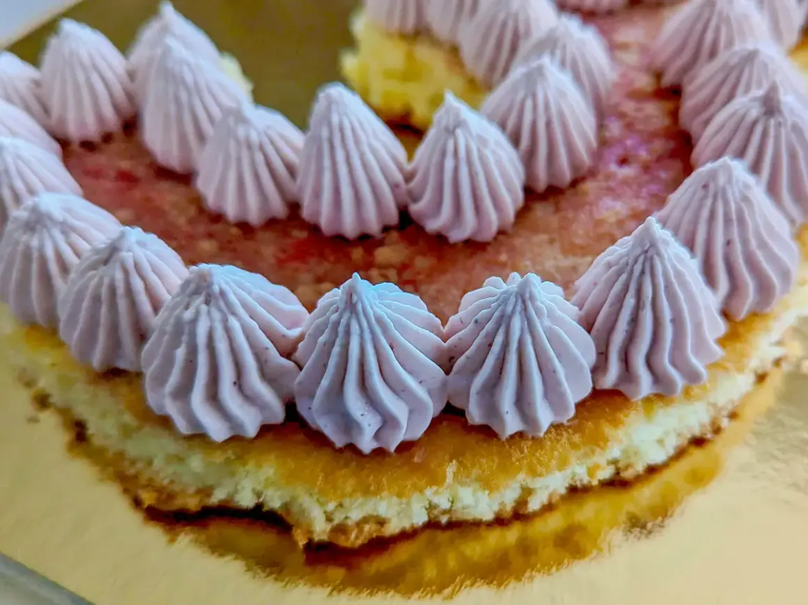 Gâteau orné de rosaces de ganache chocolat blanc framboise sur un lit de fruits rouges.