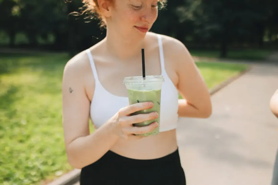 Une jeune femme aux taches de rousseur tient une boisson verte glacée, un rituel quotidien pour elle : boire du matcha.