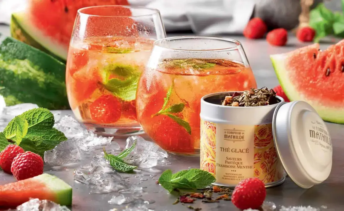 Deux verres de thé glacé maison aux fruits rouges et menthe, accompagnés de pastèque, framboises et d'une boîte de thé.