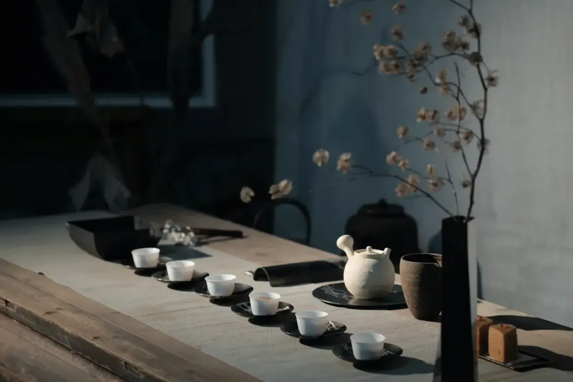 Service à thé minimaliste avec tasses blanches alignées. Une théière en céramique et un vase de fleurs séchées évoquent l'art de comment conserver le thé.
