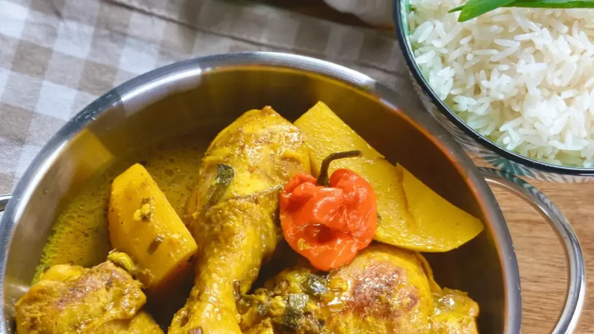 Un plat de poulet au curry, parfumé par l'épice colombo, avec des morceaux de patate douce et un piment rouge. Servi avec du riz blanc.