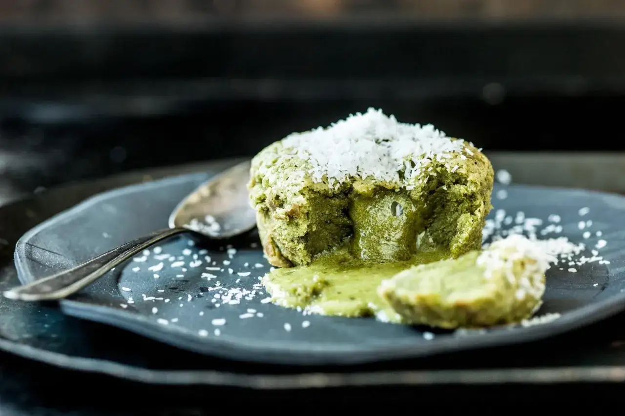 G&acirc;teau matcha chocolat blanc coulant, saupoudr&eacute; de noix de coco r&acirc;p&eacute;e sur une assiette sombre.