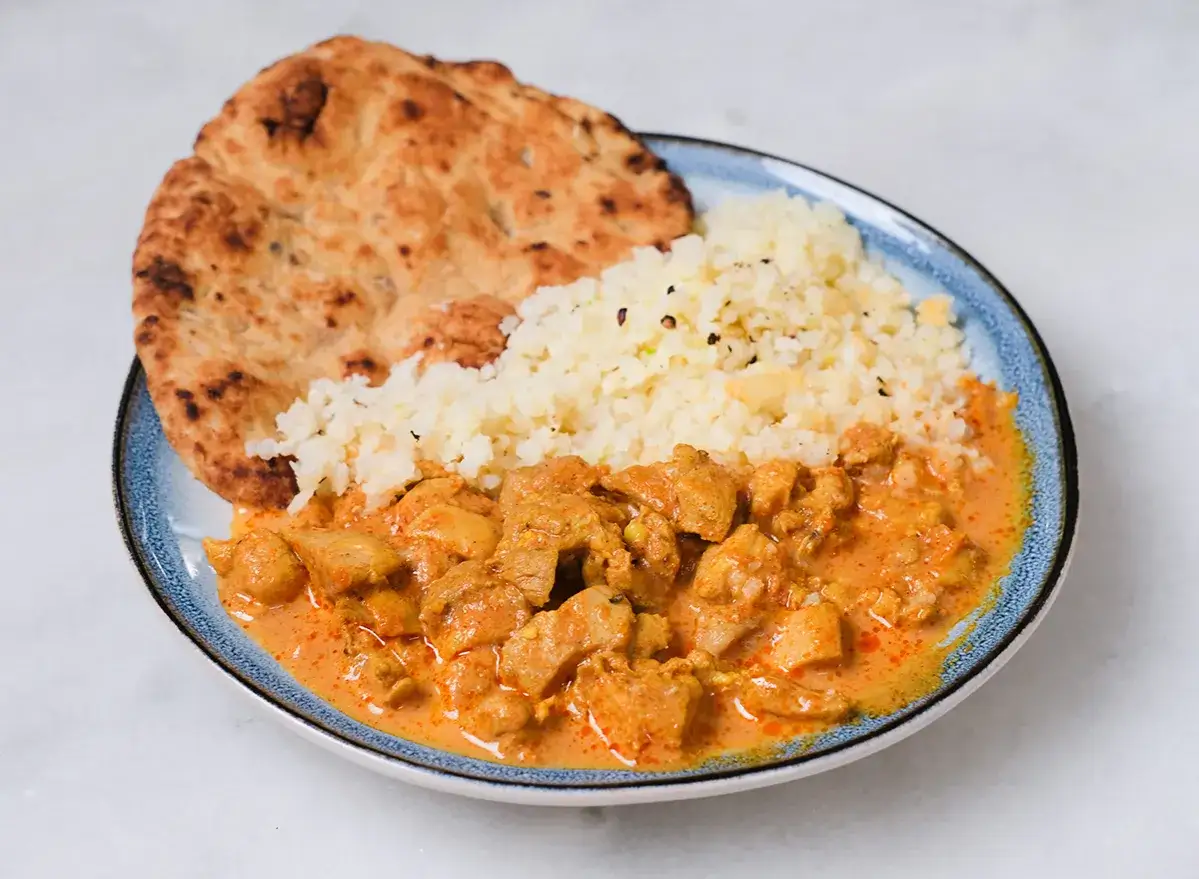 Un plat de poulet tikka massala cr&eacute;meux avec du riz et du pain naan sur une assiette bleue.