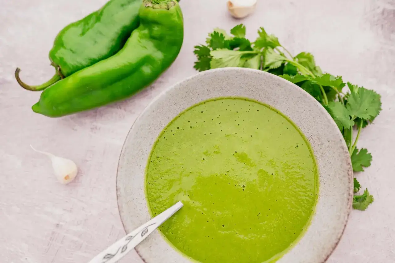 Sauce mojo verde vibrante dans un bol, avec des poivrons verts, de l'ail et de la coriandre frais &agrave; proximit&eacute;.