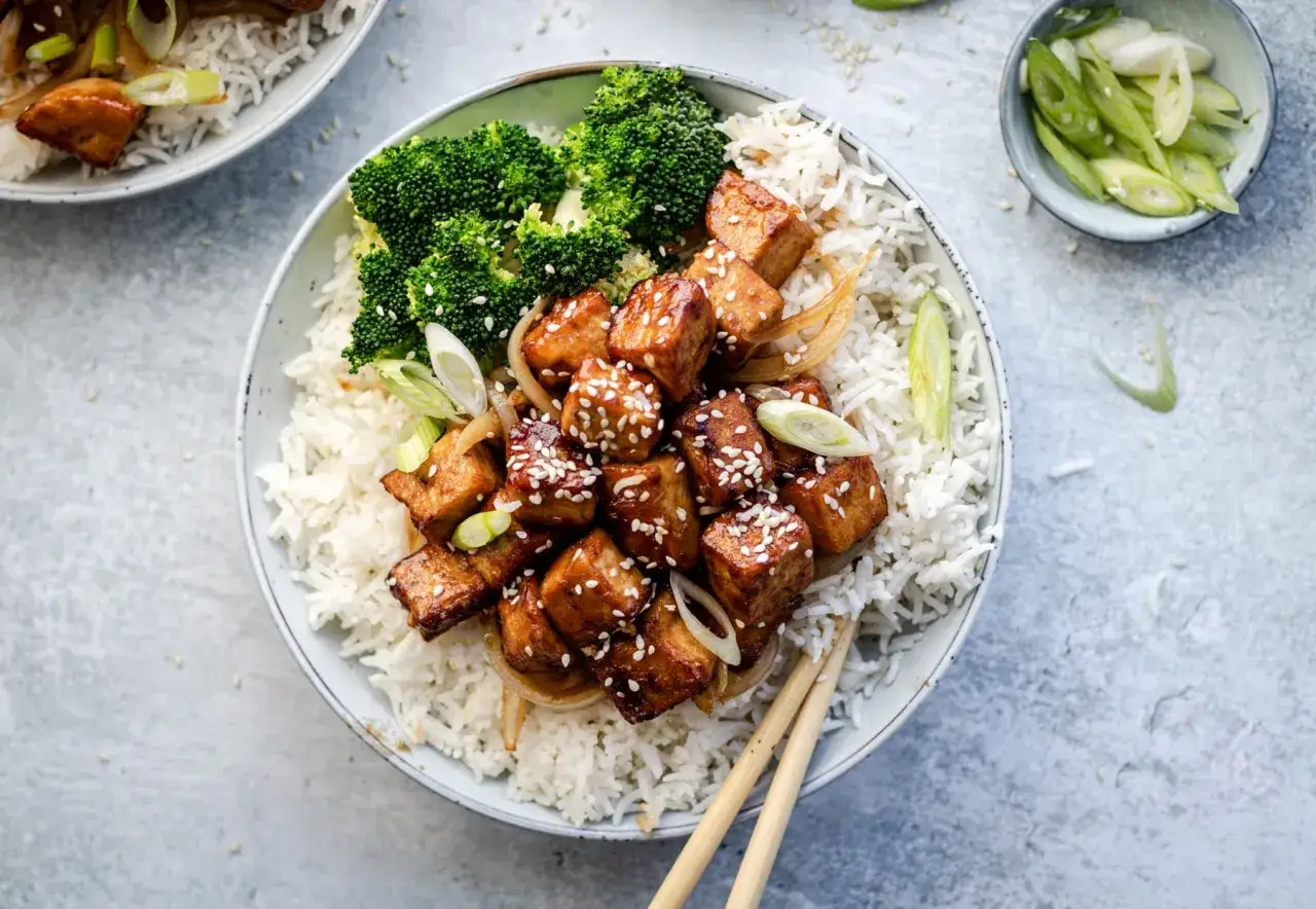 Un bol de riz blanc garni de cubes de tofu teriyaki brillants, de brocolis verts et d'oignons verts. Des graines de s&eacute;same pars&egrave;ment le plat.