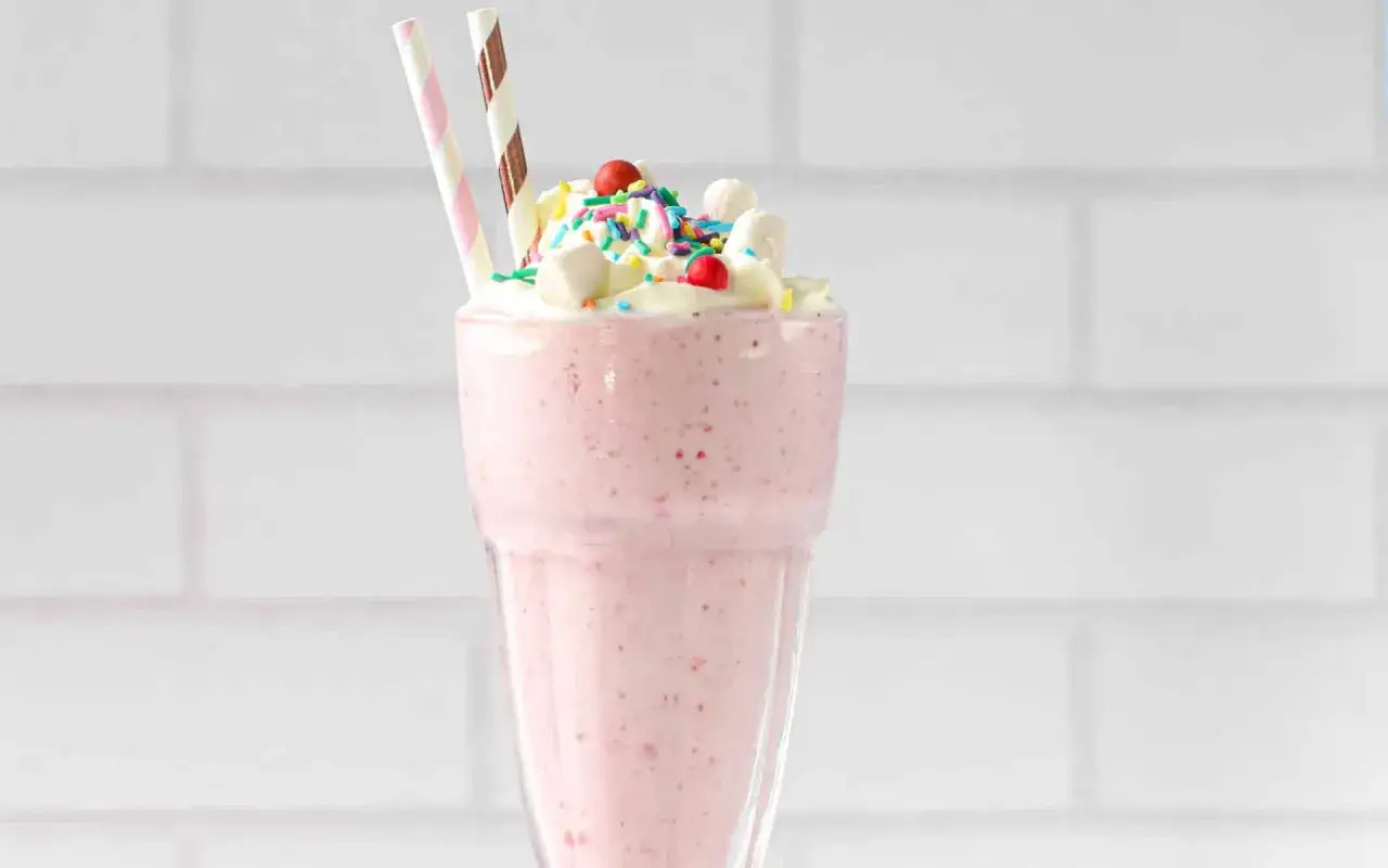 Un d&eacute;licieux milkshake vegan rose, garni de cr&egrave;me fouett&eacute;e, de mini-guimauves, de vermicelles color&eacute;s et de cerises.