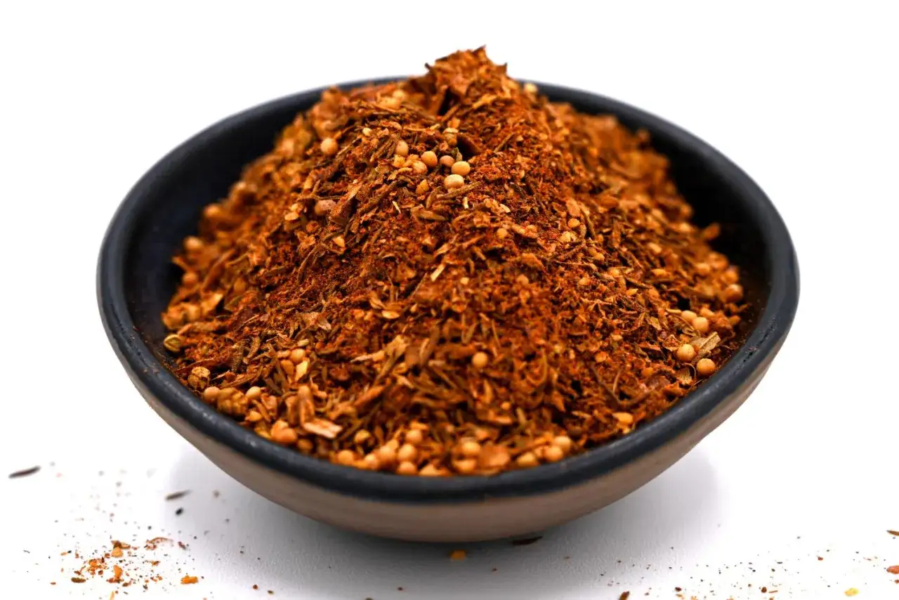 Un bol rempli d'épice cajun, un mélange vibrant de rouge et de brun avec des graines de moutarde.