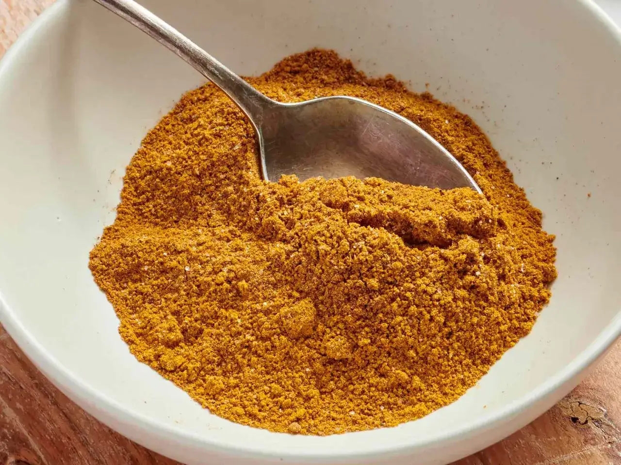 Une cuill&egrave;re remplit un bol de poudre dor&eacute;e, un m&eacute;lange parfum&eacute; de cumin et curcuma, pr&ecirc;t &agrave; relever vos plats.