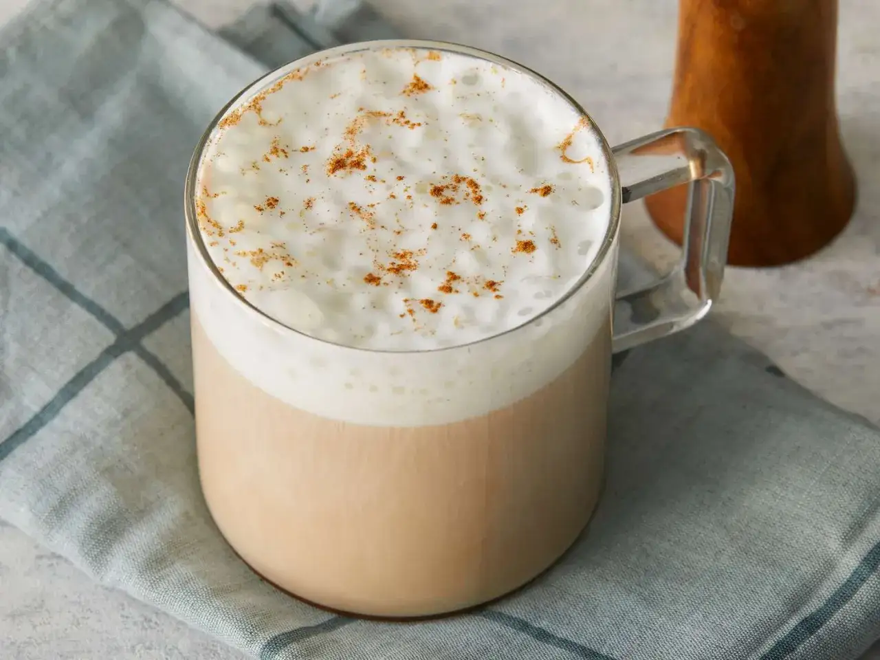 Un délicieux chai latte crémeux, saupoudré de cannelle, dans un mug en verre. Parfait pour une pause réconfortante.