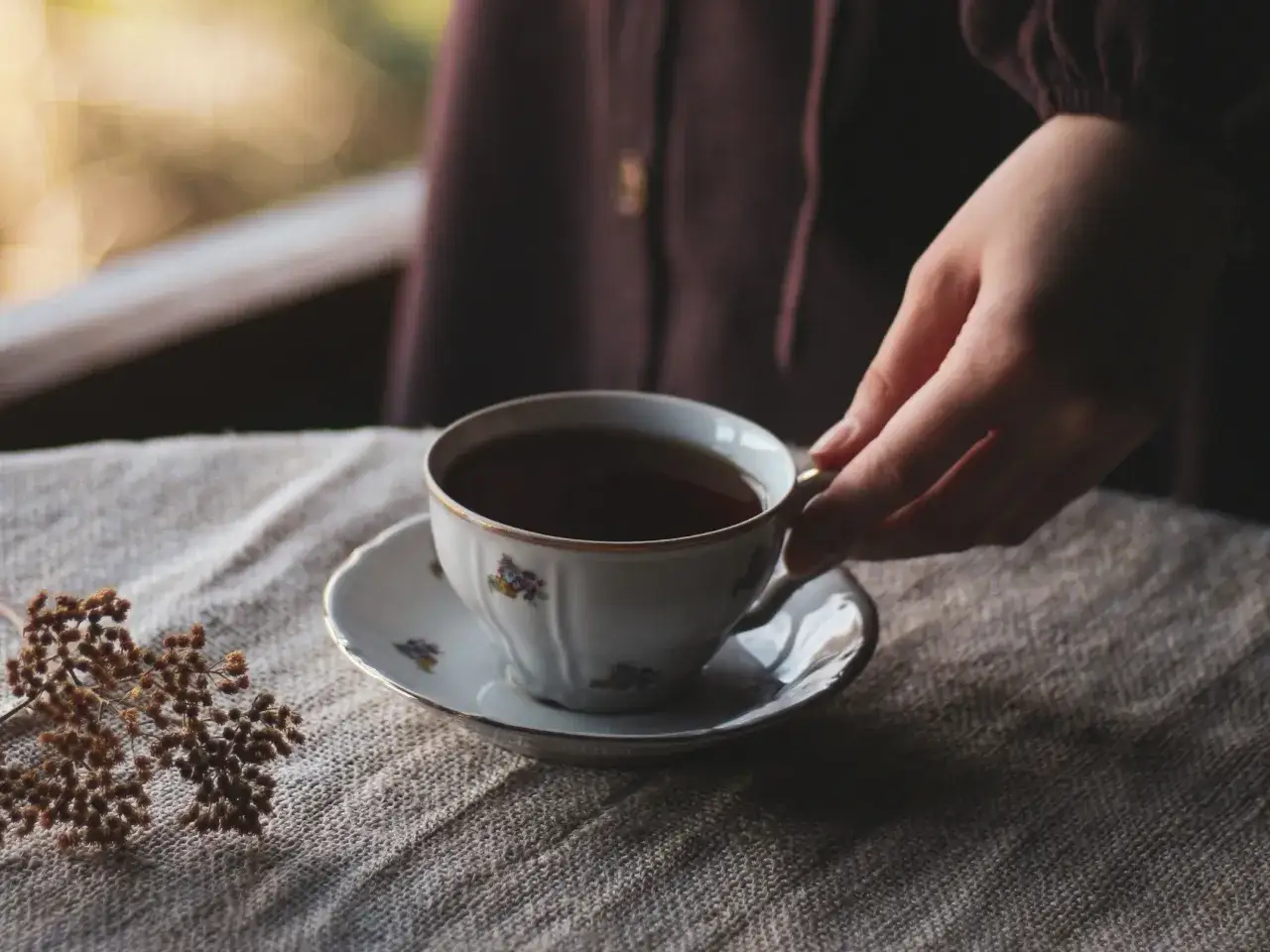 Une main saisit une tasse de thé ornée de fleurs, un moment de quiétude qui célèbre la culture du thé.