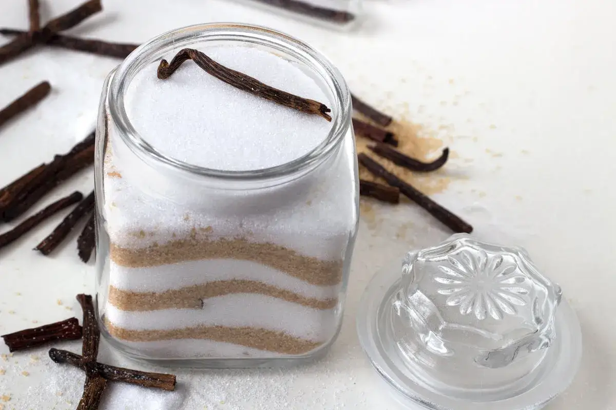 Un bocal de sucre vanillé maison, avec des gousses de vanille et du sucre roux.