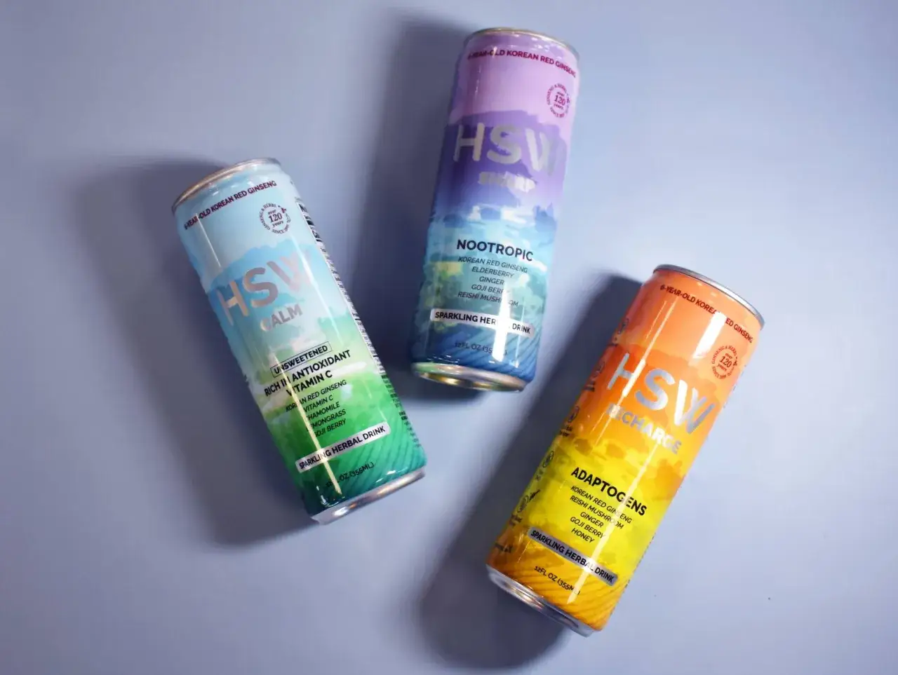 Trois canettes de boissons p&eacute;tillantes aux herbes, chacune mettant en avant le ginseng rouge cor&eacute;en et le gingembre pour un coup de pouce naturel.
