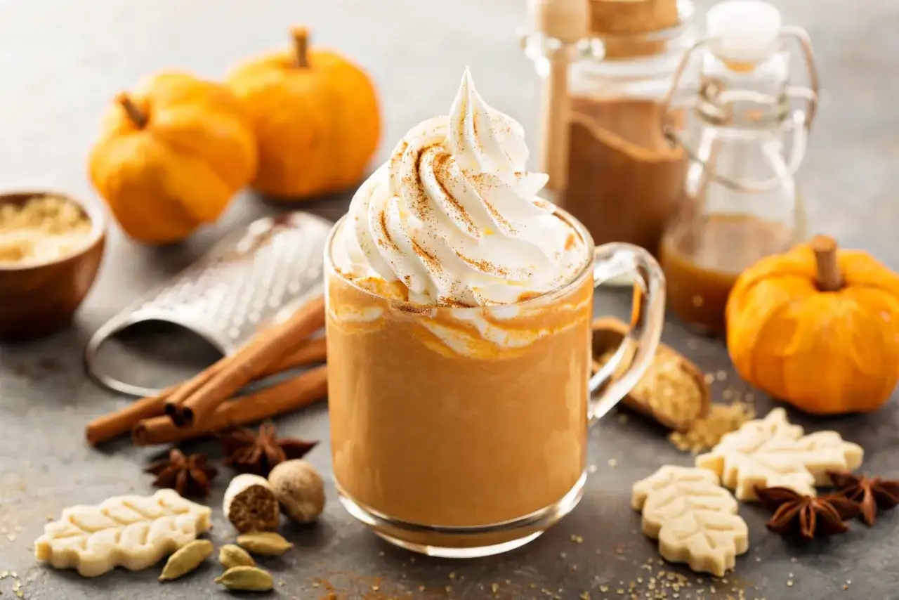 Une boisson automne r&eacute;confortante, garnie de cr&egrave;me fouett&eacute;e et de cannelle, entour&eacute;e de citrouilles miniatures et d'&eacute;pices.